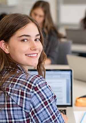 Teen smiling while working on laptop at school